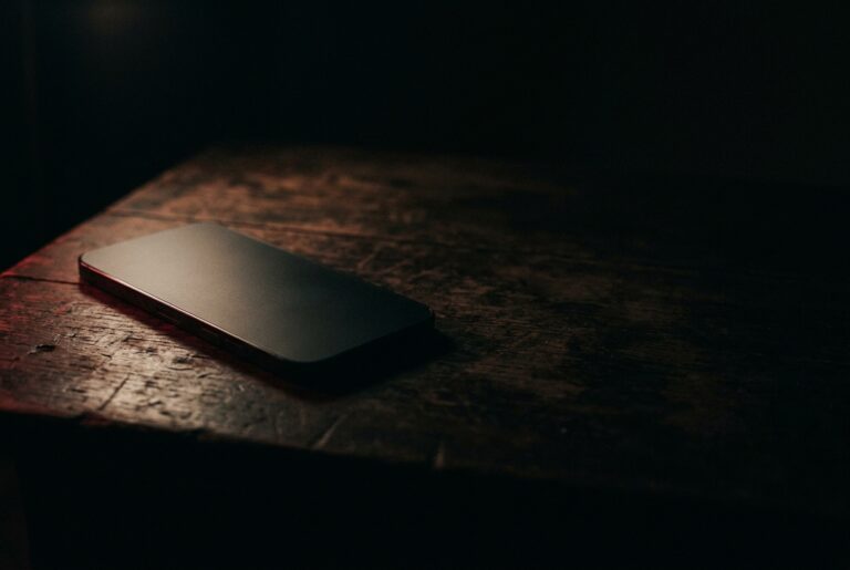 暗い机の上に伏せて置かれたスマートフォンと、縁だけに乗る光