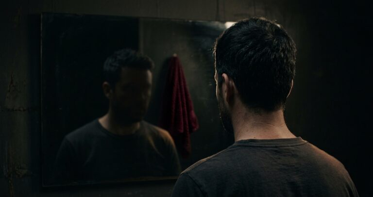 低い照明の下、鏡に映る男性の後頭部から肩にかけてのシルエット